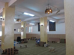 A mostly empty room with stools, chairs, and cushions strewn about; on the wall are texts in Samaritan Hebrew