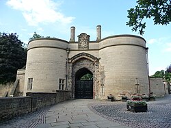 Low angle shot from the former moat now grassed over, looking up at twin stone towers with an arched bridge accessing the entrance to the right