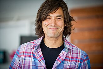 David Usher wearing a black t-shirt underneath a light checkered shirt, smiling at camera