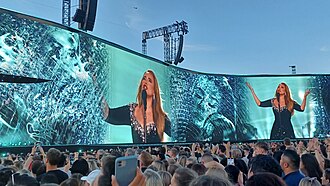 Adele appears on a blue-green background on a giant screen