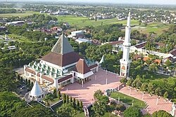 An aerial view of a mosque with one minaret and pointed pyramidal roof