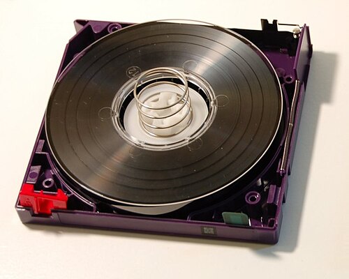 LTO-2 cartridge with the top shell removed, showing the internal components. Top right corner: tape access gate. Bottom left corner: write-protect-tab. Bottom right corner: cartridge memory chip