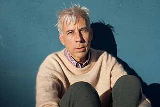 John Vanderslice sitting in front of a teal blue wall