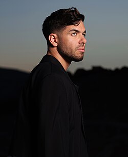 Profile image of Matteo Milleri wearing dark clothing, looking up and to the right in front of a blurry twilit background