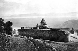 An old black and white photo of a stone monastery with rounded domes built against a hillside.