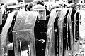 A "long shield" Police Support Unit, equipped with protective riot gear and acrylic shield. "Short shield" units were equipped with smaller, round shields which afforded greater mobility (1985).