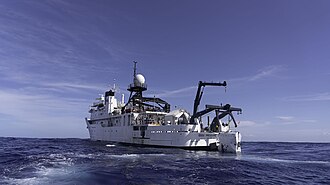 A large support vessel with a small rectangular profile deep submergence vehicle suspended over the water at the stern