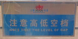 A light-colored sign with Chinese characters and "Note that the level of gap" written on it in blue