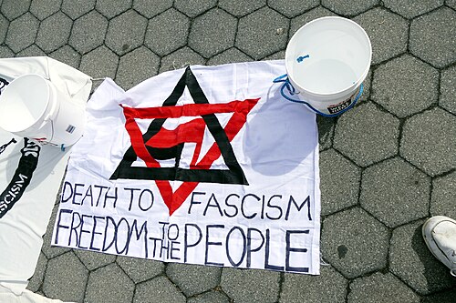 banner shows a Star of David made from a red triangle pointing down and a black triangle pointing up, the antifascist red and black flags a are in the center, and text under it says "death to fascism, freedom to the people"