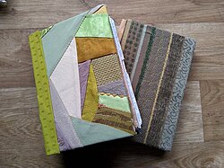 Two handmade, hardbacked, fabric covered junk journals with one angled on top of the other so both are visible.