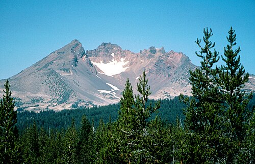A volcano with a large crater rises above a forested region.