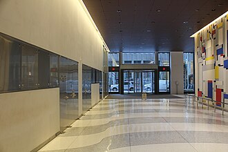 View of the lobby, facing south toward 50th Street, along the passageway on the eastern side of the elevator core. There are white and gray pavers on the floor. To the right is a wall with the artwork "Relational Painting No. 88", a multicolored art piece with geometric shapes.