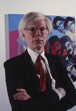 Warhol crossing his arms while looking at a camera