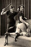 A woman spanking another woman with a violin bow, a notably unconventional implement