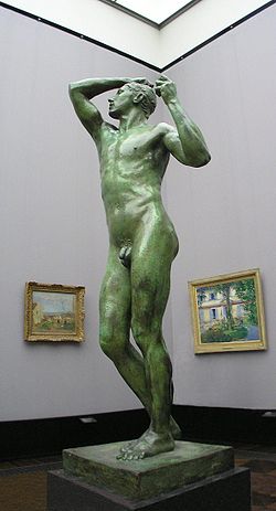 Life-sized nude stature of a male on a pedestal on display in a museum.