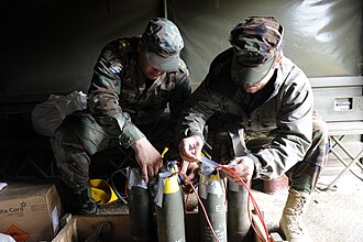 A group of 105 mm artillery shells with plastic explosive stuffed into their fuze pockets to act as booster charges. Each of the five shells has been linked together with red detcord to make them detonate simultaneously.