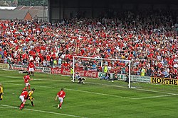Football game; goalie misses the ball, large crowd in background, many with visible reactions to the goal