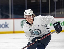 Ice hockey player in a white Seattle Kraken skating with his stick in his hands