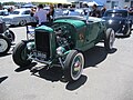 Hi-boy Deuce roadster with a flathead V8 (with factory head and exhaust but aftermarket alternator ignition and dual-carb intake), dropped tube axle, and drum brakes.