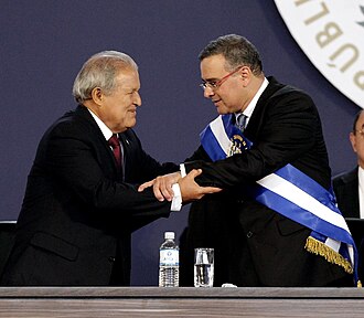 A photograph of Mauricio Funes wearing the presidential sash with Salvador Sánchez Cerén