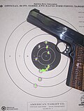 Handgun and paper target showing grouping of ten shots