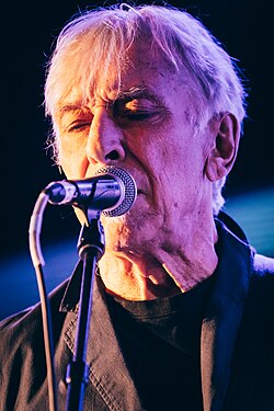 Cale singing into a microphone onstage