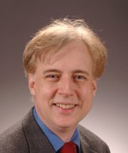 Headshot of a suited Benner on a dull background