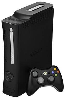 Close up photograph of a black video game console facing to the left as it stands upright on its side. The front has a silver disc tray cover and recessed section with a concave button. A black wireless video game controller sits next to the console.