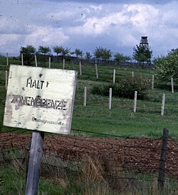 The "second-generation" fences in 1962, with derelict barbed wire in the foreground, a control strip, two rows of barbed wire further back and a watchtower at the rear