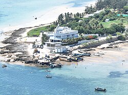 Aerial photograph of a beachfront hotel in Vilankulo, surrounded by palm trees, boats and shallow turquoise water.