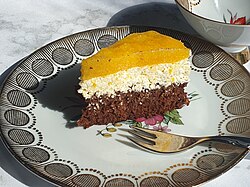 A slice of Fanta cake served on a decorated plate. It is a three-layered sponge cake, where the top orange layer is made from Fanta.