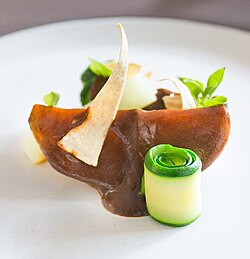 A slice of squash covered with a sauce and garnished with basil sprouts and a tortilla chip.