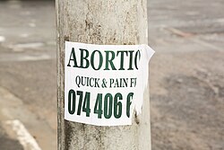 Torn flier on a pole reading: ABORTION / QUICK & PAIN FREE / 074 406 6 [rest of number illegible]
