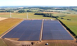 Aerial view of a solar farm with part of a wind farm in the background