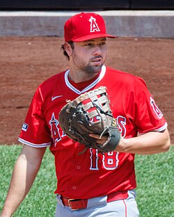 A man in a read baseball jersey and red baseball hat holds a baseball glove up in front of his chest.