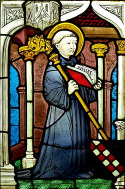Stained glass image of a kneeling man with a halo holding an open book and a staff