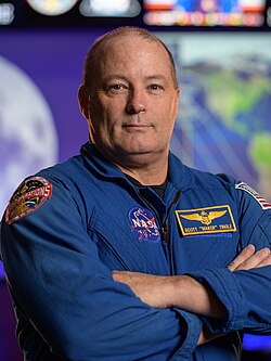 A man in a blue flight suit; he is facing the camera and smiling.