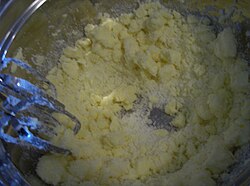 A metal mixing bowl, with chunks of butter and white sugar