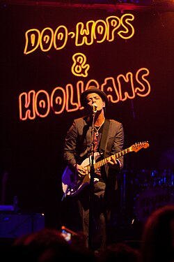 Mars, in a black suit and hat, playing guitar onstage