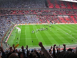 A full football stadium, with spectators in the left half wearing blue, and those in the right half wearing red