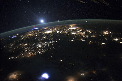 A sprite at the horizon, with lightning below in the troposphere and above the green line of airglow at the upper mesopause and border to space (the bright light above is the Moon).