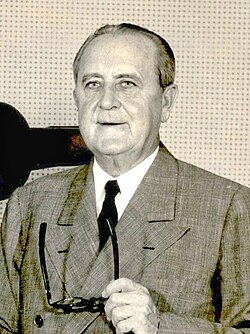 Niles Trammell, holding a pair of glasses in his left hand, standing next to a television camera with labels for "WCKT" and "RCA Television" on it