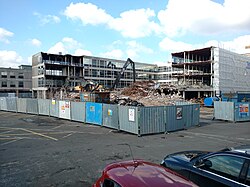 Fenced off site with four storey part demolished office type building having external cladding removed exposing metal framework