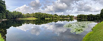 A small lake surrounded by trees with a large house on the far side