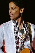 Prince looks away at a concert as he dons white-colored clothing.