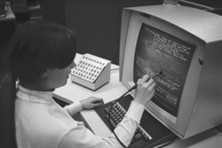 A black and white photo from 1969 showing a person holding a light pen up to an computer screen.