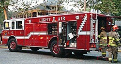 A very large red fire truck with white ribbon-like accents is parked and firefighters are unloading things from it.