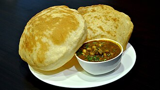 A bowl of chickpea curry on a plate with two large, puffy flatbreads.
