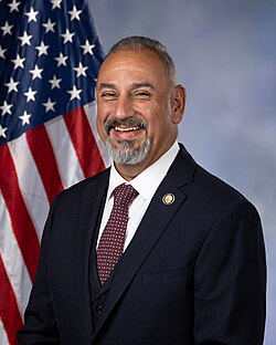 Official House portrait of Cisneros in front of the U.S. flag, wearing a black suit, white shirt, and checkered red tie.