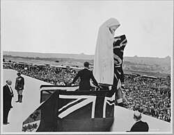 A figure standing on flag-covered stage in front of the statue of Canada Bereft